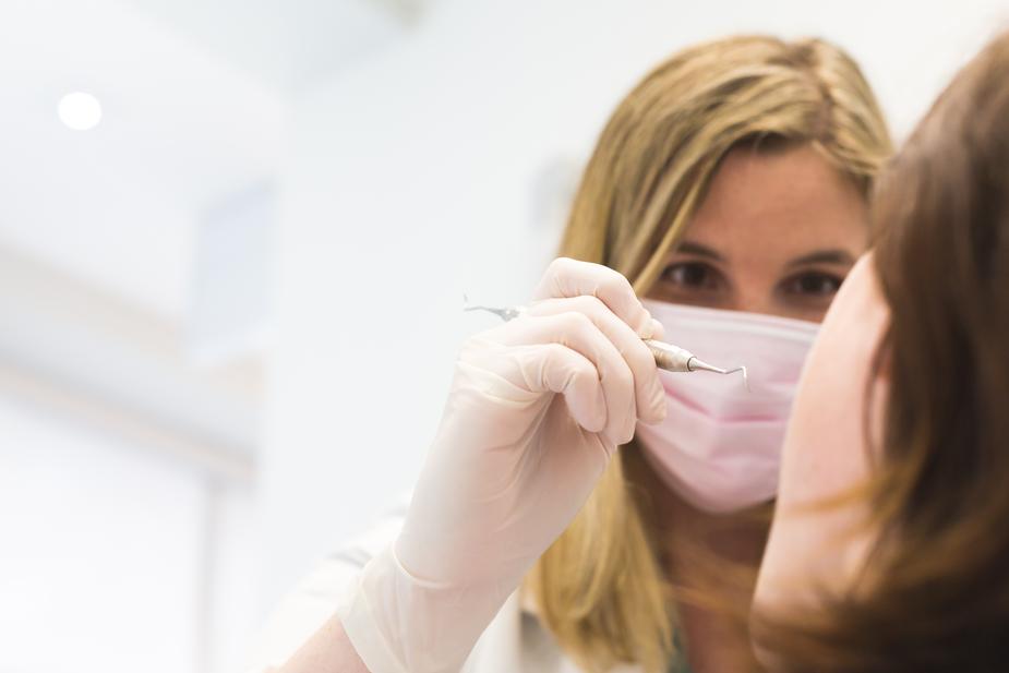 Une dentiste avec un outil de nettoyage, un masque médical et des gants de vinyle qui examine la bouche d'une femme